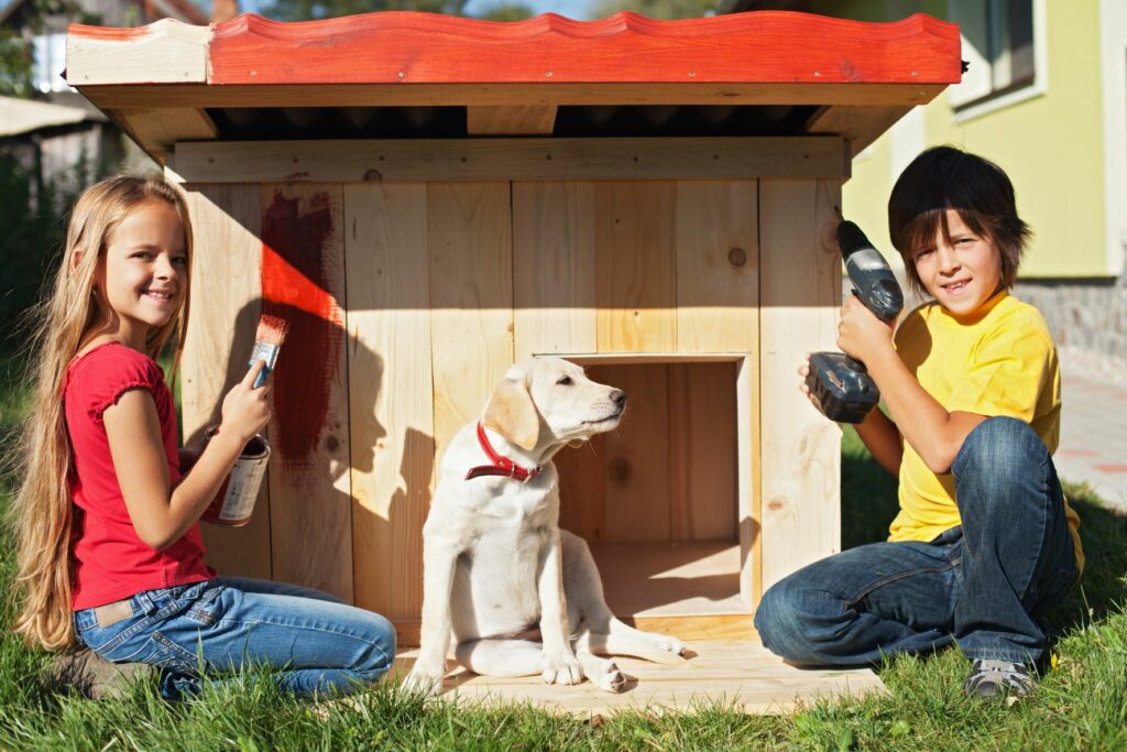 Duas crianças e um cão junto a uma casota para cães